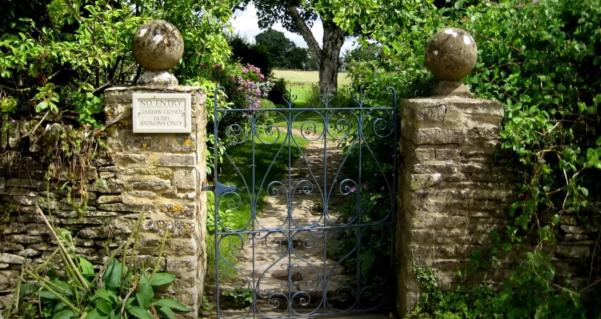 Historic stone gate entrance with ornate ironwork surrounded by mature trees and professional landscaping