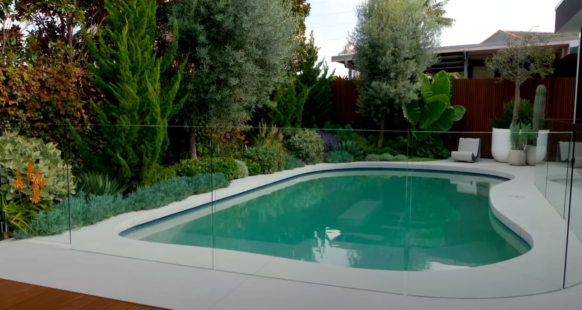 Modern pool area with glass fencing, tropical plants, and contemporary landscape design